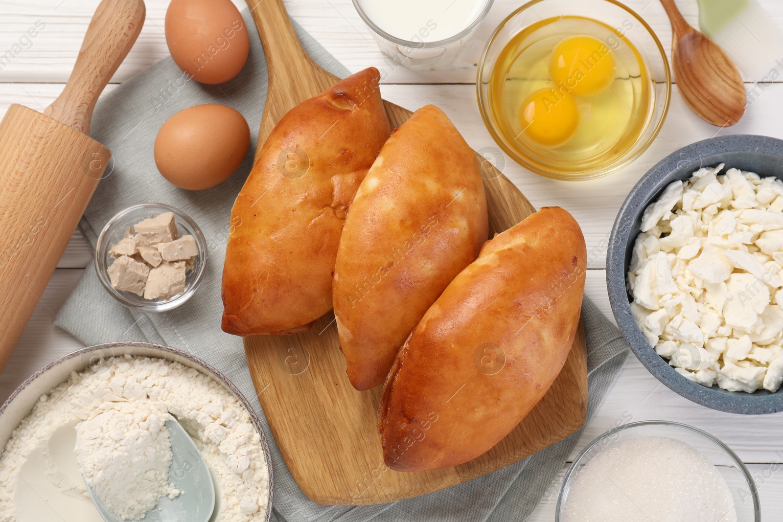 Photo of Delicious pirozhki (stuffed pastry pies) and ingredients on white wooden table, flat lay