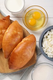 Photo of Delicious pirozhki (stuffed pastry pies) and ingredients on white wooden table, flat lay