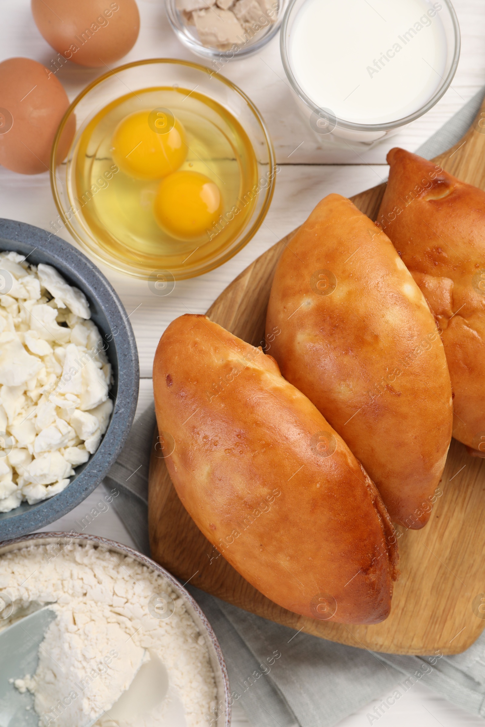 Photo of Delicious pirozhki (stuffed pastry pies) and ingredients on white wooden table, flat lay