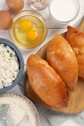 Photo of Delicious pirozhki (stuffed pastry pies) and ingredients on white wooden table, flat lay