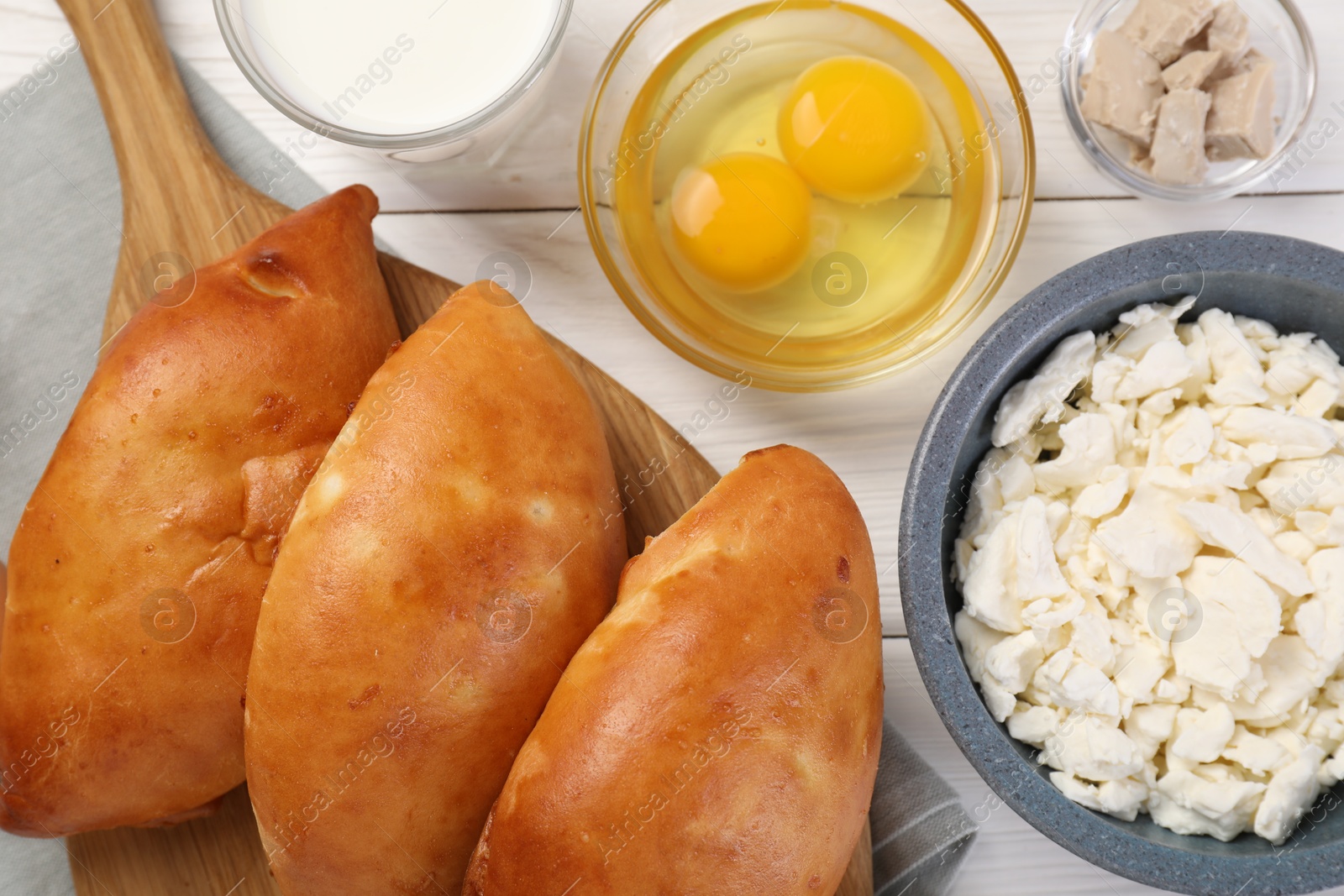 Photo of Delicious pirozhki (stuffed pastry pies) and ingredients on white wooden table, flat lay