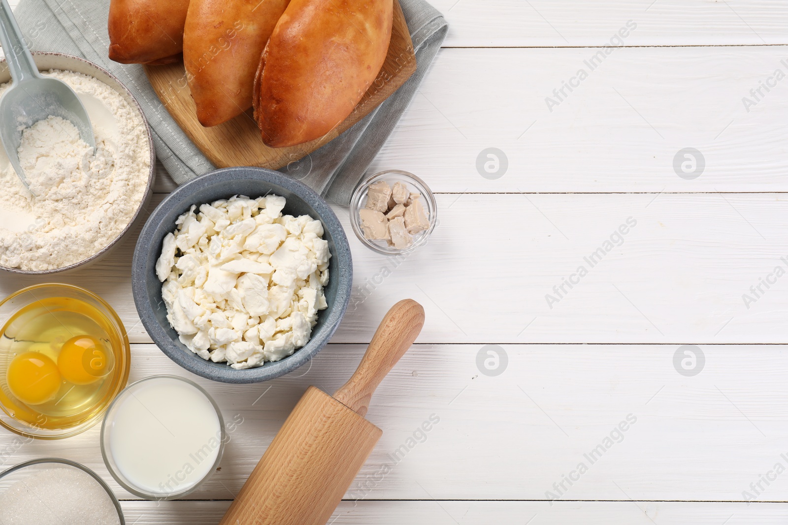 Photo of Delicious pirozhki (stuffed pastry pies) and ingredients on white wooden table, flat lay