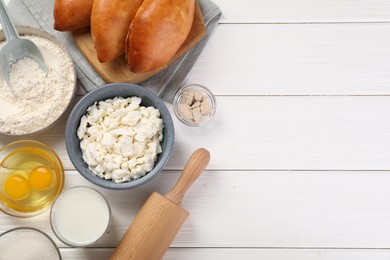 Photo of Delicious pirozhki (stuffed pastry pies) and ingredients on white wooden table, flat lay