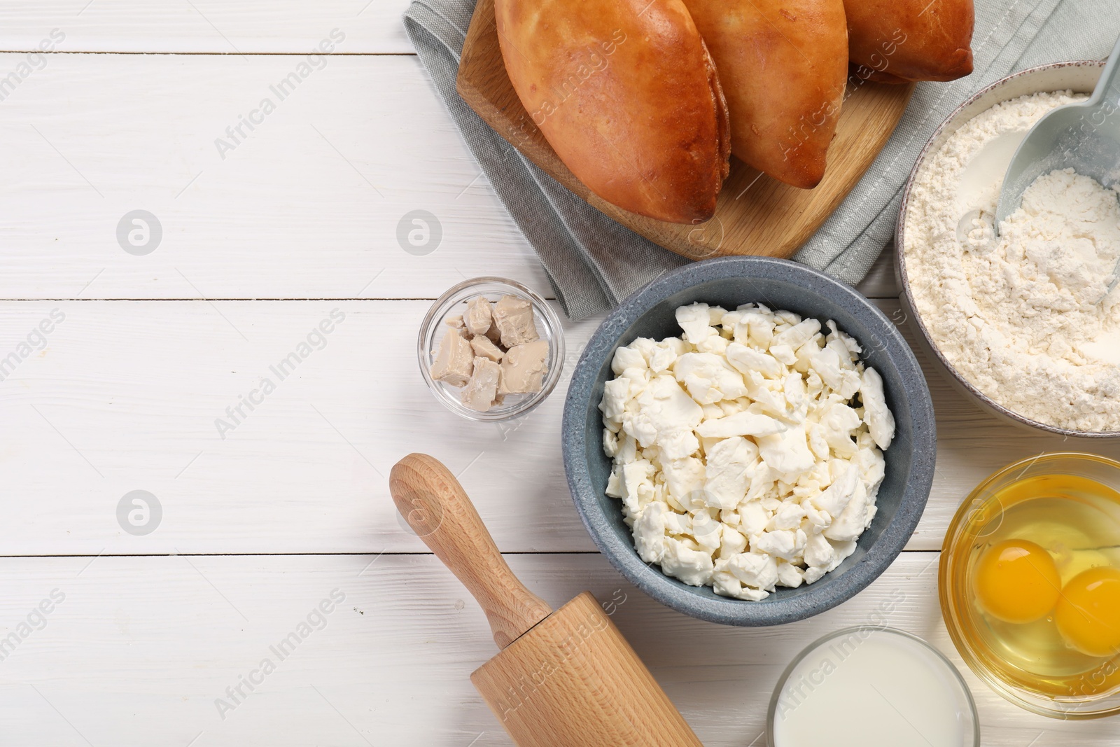 Photo of Delicious pirozhki (stuffed pastry pies) and ingredients on white wooden table, flat lay