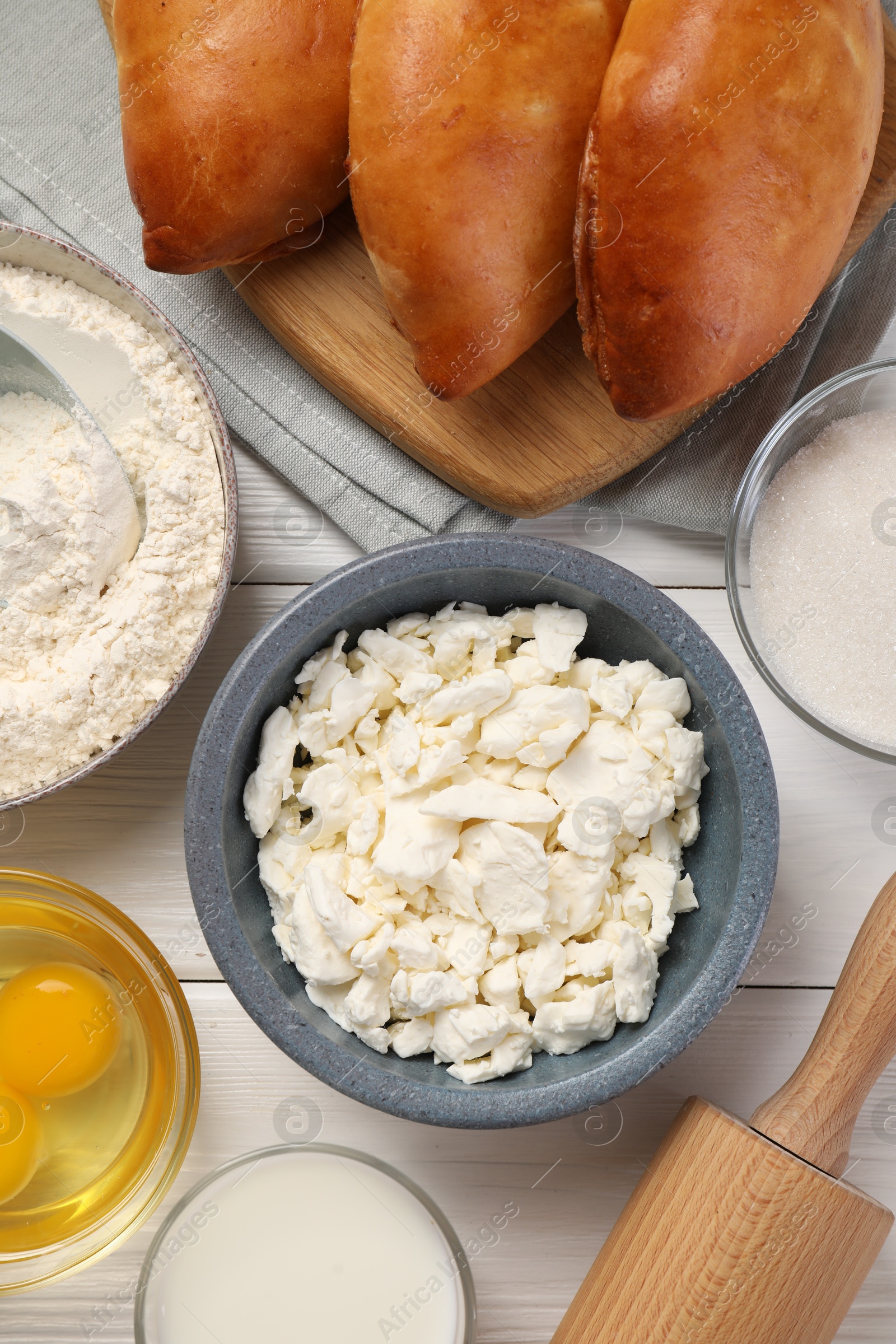 Photo of Delicious pirozhki (stuffed pastry pies) and ingredients on white wooden table, flat lay