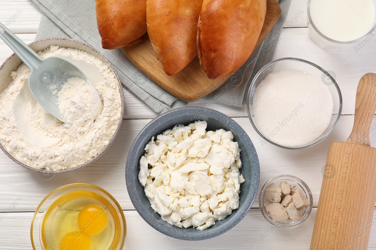 Photo of Delicious pirozhki (stuffed pastry pies) and ingredients on white wooden table, flat lay