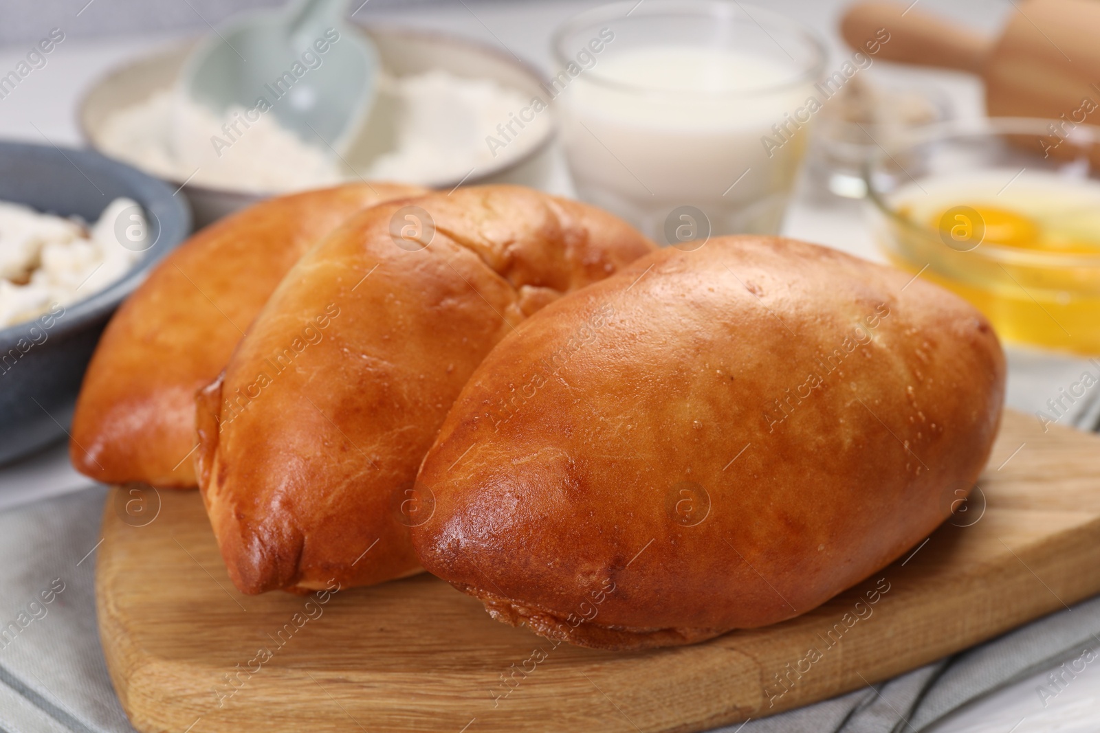 Photo of Delicious pirozhki (stuffed pastry pies) and ingredients on white wooden table, closeup