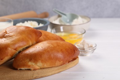 Photo of Delicious pirozhki (stuffed pastry pies) and ingredients on white wooden table, closeup