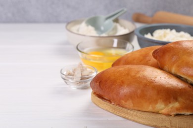 Photo of Delicious pirozhki (stuffed pastry pies) and ingredients on white wooden table, closeup