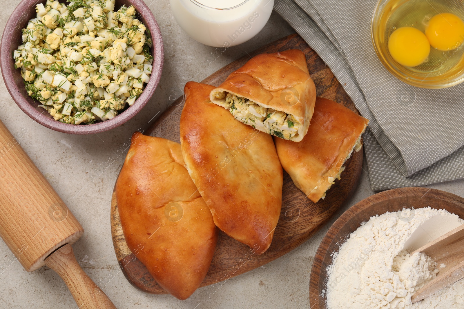 Photo of Delicious pirozhki (stuffed pastry pies) and ingredients on grey table, flat lay