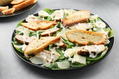 Photo of Delicious Caesar salad with chicken on grey textured table, closeup