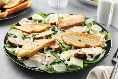 Photo of Delicious Caesar salad with chicken on grey textured table, closeup