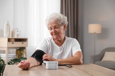 Photo of Senior woman measuring blood pressure at wooden table indoors