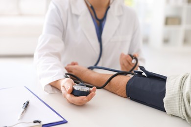 Photo of Doctor measuring patient's blood pressure at table in hospital, closeup