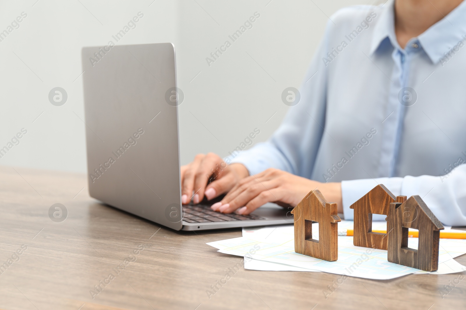 Photo of House hunting. Woman with laptop, papers and house figures at wooden table, closeup