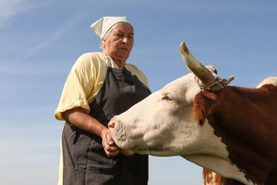 Photo of Senior woman with beautiful cow under blue sky, low angle view