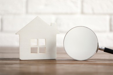 Photo of House hunting. Magnifying glass and house figure on wooden table