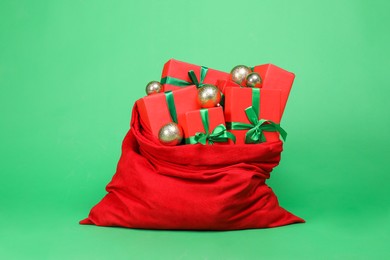 Photo of Red Santa Claus bag with baubles and gift boxes on green background