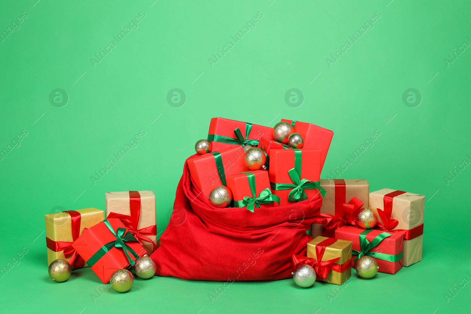 Photo of Red Santa Claus bag with baubles and gift boxes on green background