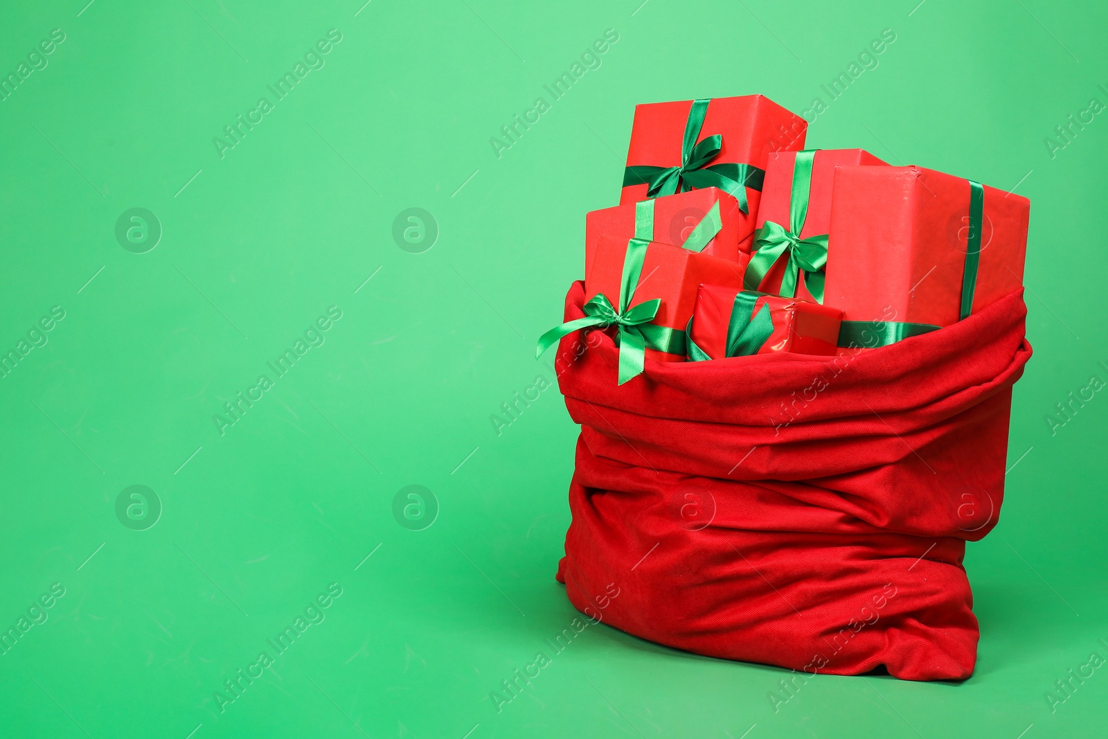 Photo of Red Santa Claus bag with gift boxes on green background, space for text