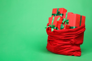 Photo of Red Santa Claus bag with gift boxes on green background, space for text