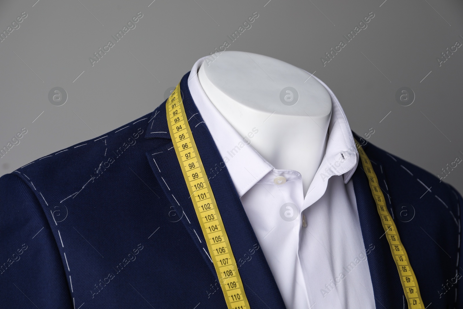 Photo of Semi-ready jacket with tailor's measuring tape and white shirt on mannequin against grey background, closeup