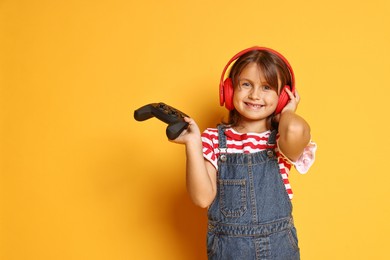 Photo of Smiling little girl in headphones with controller on orange background. Space for text