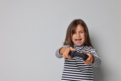 Photo of Emotional little girl playing video game with controller on grey background. Space for text