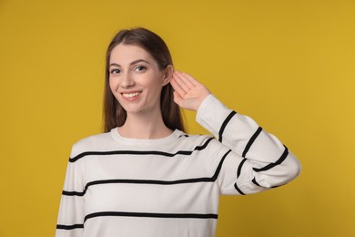 Photo of Woman showing hand to ear gesture on dark yellow background