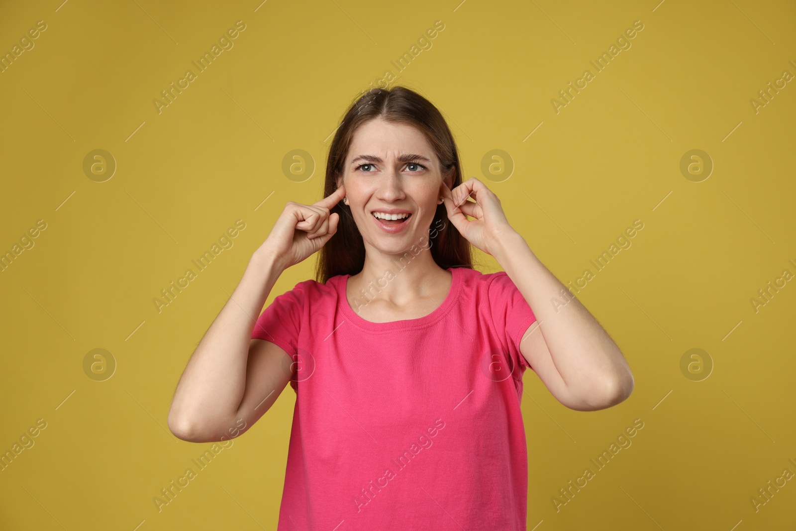 Photo of Woman covering her ears with fingers on dark yellow background