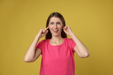 Photo of Woman covering her ears with fingers on dark yellow background