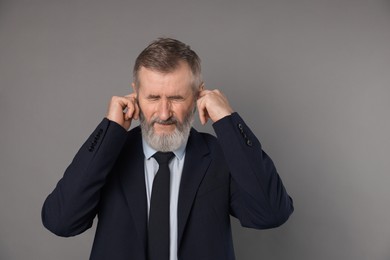 Photo of Senior man covering his ears with fingers on grey background. Space for text