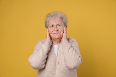 Photo of Senior woman covering her ears on dark yellow background