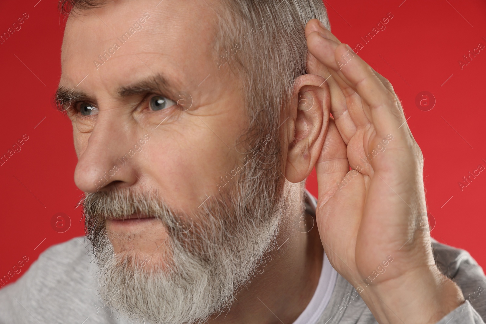 Photo of Senior man showing hand to ear gesture on red background, closeup