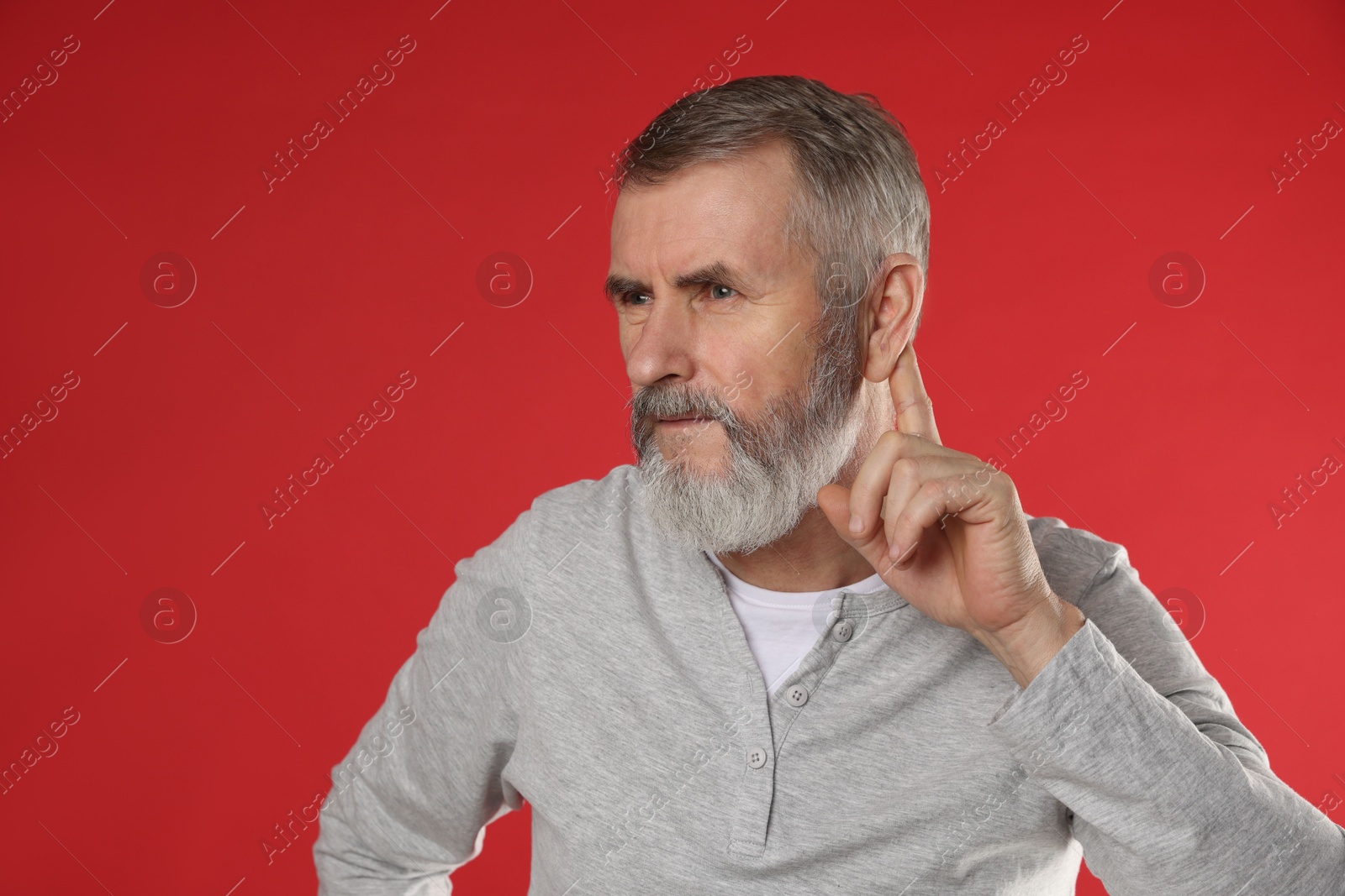 Photo of Senior man showing hand to ear gesture on red background