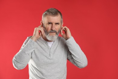 Photo of Senior man covering his ears with fingers on red background. Space for text