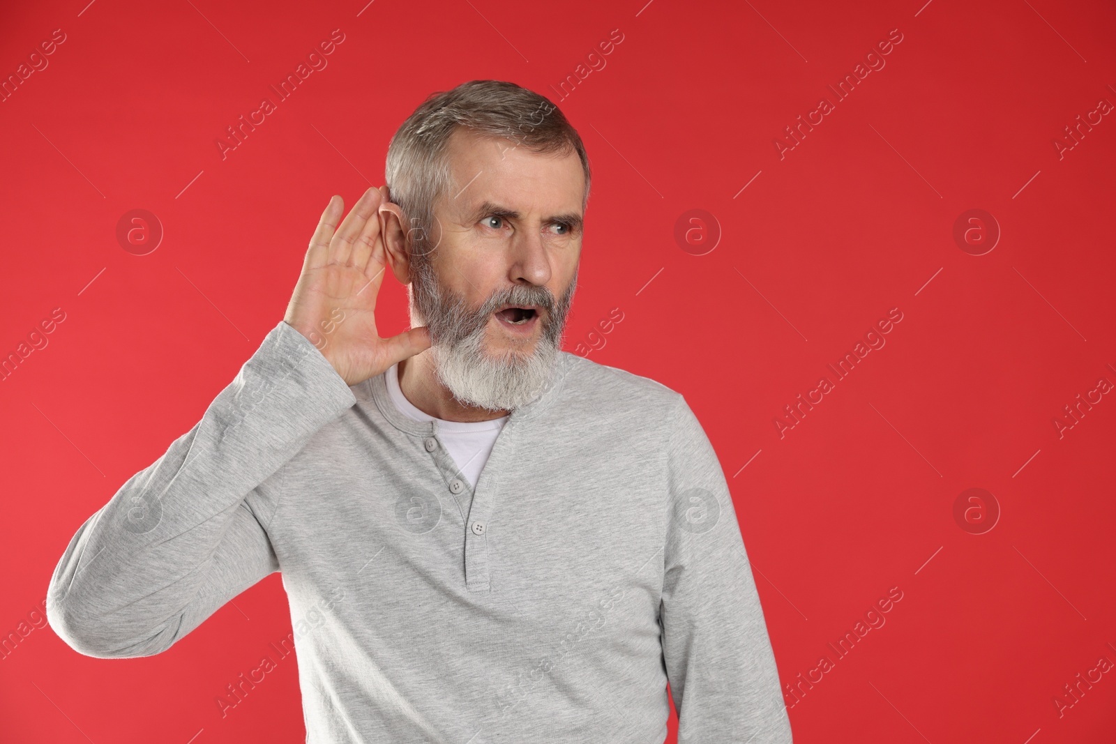 Photo of Senior man showing hand to ear gesture on red background. Space for text