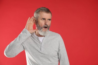 Photo of Senior man showing hand to ear gesture on red background. Space for text