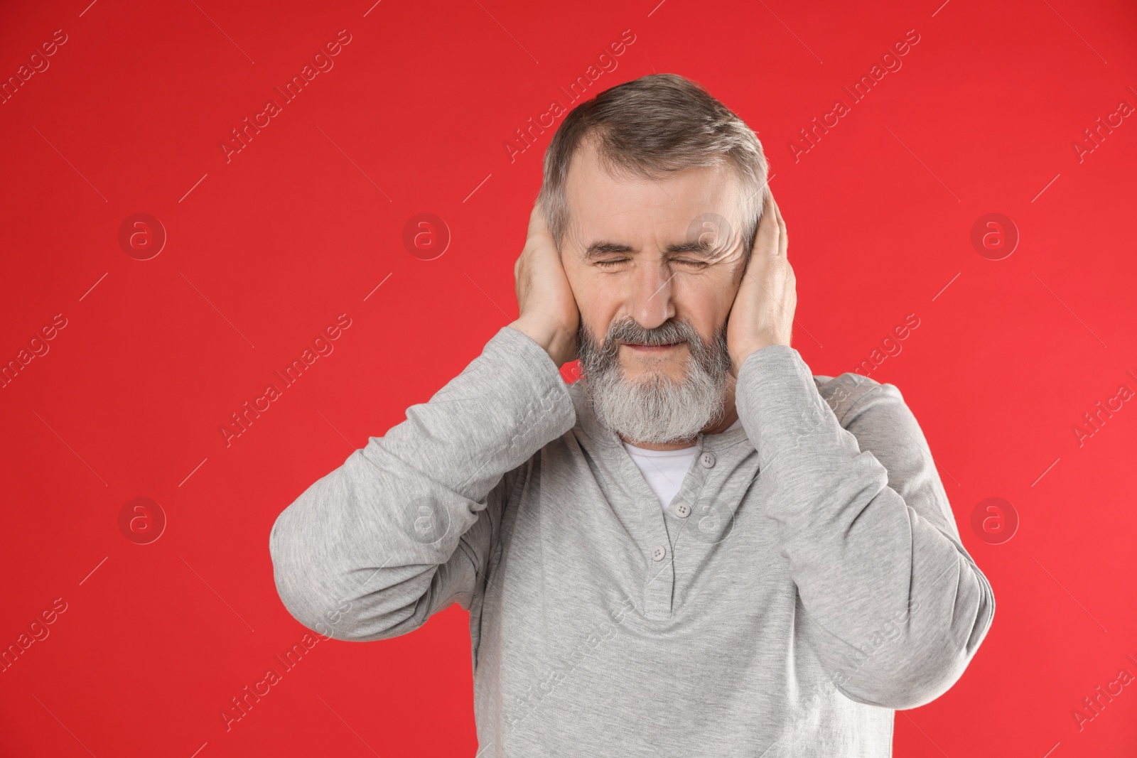 Photo of Senior man covering his ears on red background