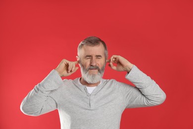 Photo of Senior man covering his ears with fingers on red background