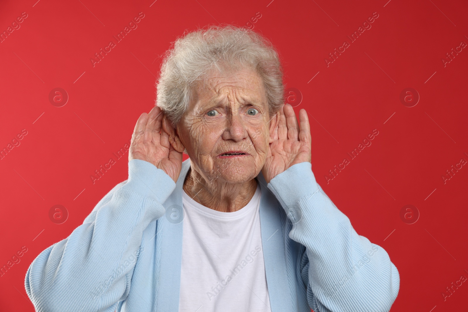 Photo of Senior woman showing hand to ear gesture on red background