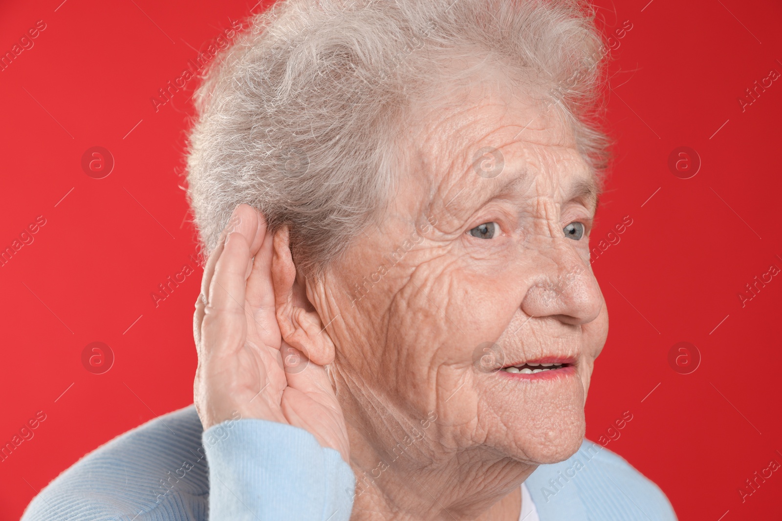 Photo of Senior woman showing hand to ear gesture on red background, closeup