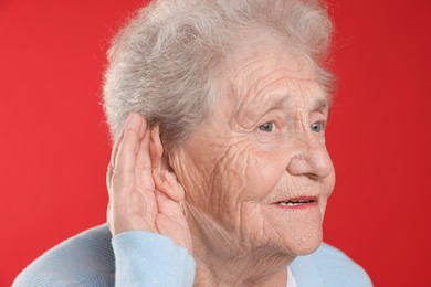 Photo of Senior woman showing hand to ear gesture on red background, closeup