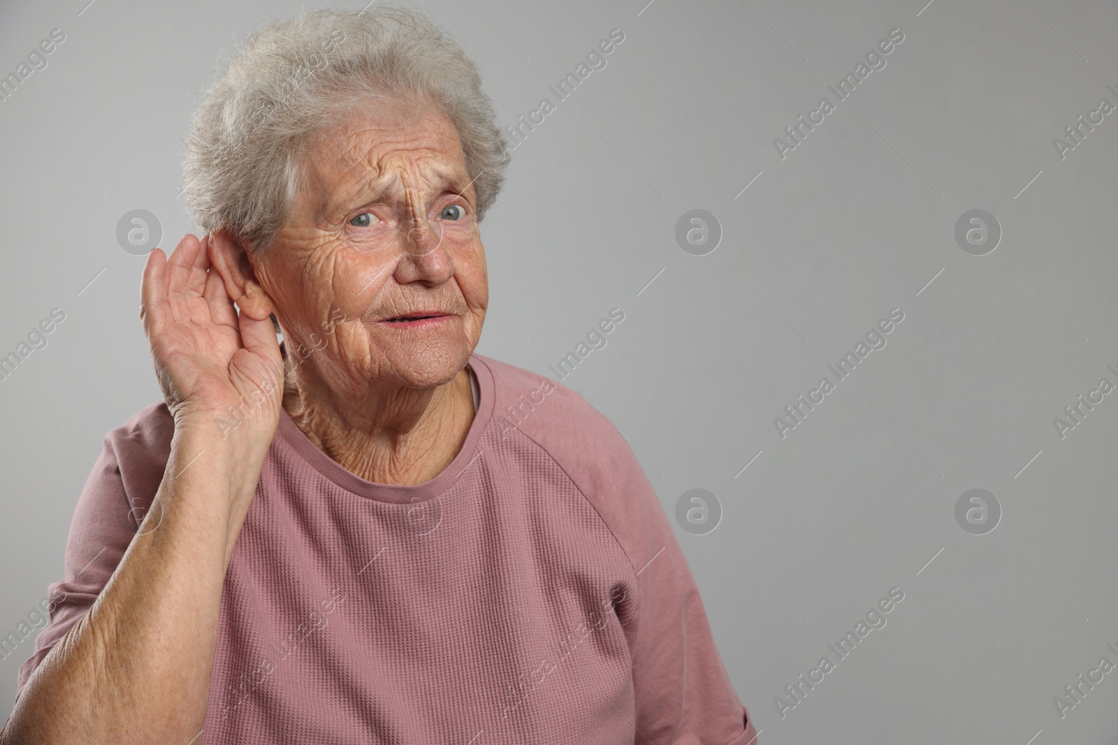 Photo of Senior woman showing hand to ear gesture on grey background, space for text