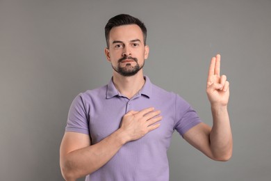 Photo of Man showing oath gesture on grey background. Making promise