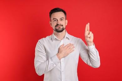 Photo of Man showing oath gesture on red background. Making promise