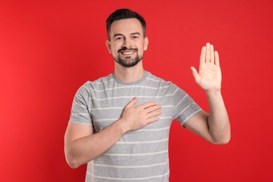 Photo of Man making promise with raised hand on red background. Oath gesture