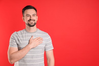 Photo of Man making promise on red background, space for text. Oath gesture