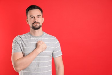 Photo of Man making promise on red background, space for text. Oath gesture