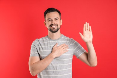 Photo of Man making promise with raised hand on red background. Oath gesture